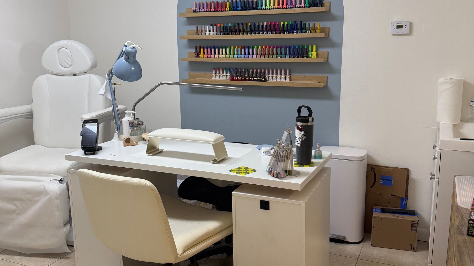 The Nail Days manicure station in front of a powder-blue arch lined with shelves of gel polish